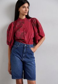 Punainen paita, jossa on kukkakuosi, korkeat puffihihat ja nappisuljenta. Yhdistetty korkeavyötäröisiin farkkushortseihin klassisessa sinisessä värissä.