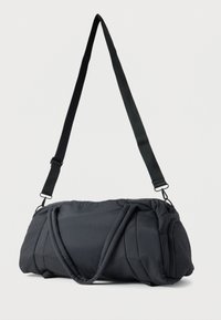 Sac polochon noir matelassé avec sangle d'épaule réglable et deux poignées courtes, posé sur un fond blanc uni.