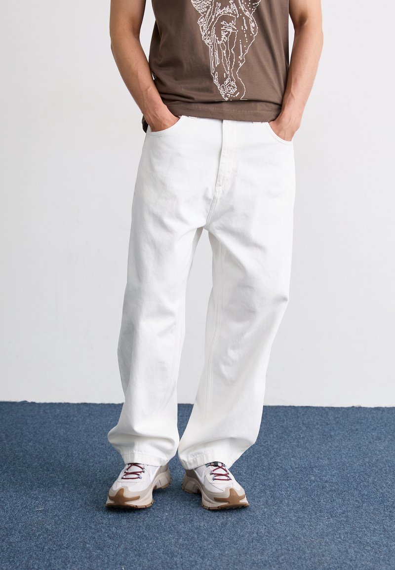 Hvite bomullsbukser med bred ben, høy midje silhuett. Kjemper med grå og beige sneakers med røde detaljer og snøring.