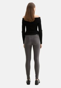 Top negro de canalé sin hombros combinado con pantalones gris ajustados. Los pantalones tienen bolsillos traseros y una textura suave, descansando sobre unos zapatos de plataforma negros.