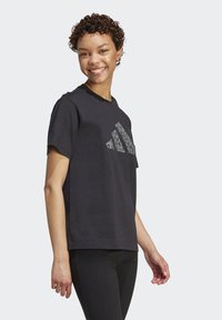 Černé bavlněné tričko s kulatým výstřihem a krátkými rukávy, na přední straně s tonálním logem Adidas se vzorem leopardí kůže.