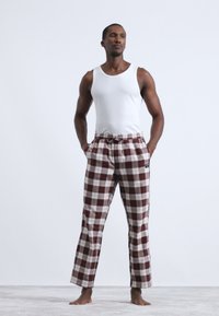 Camiseta sin mangas blanca, pantalones de chándal de cuadros marrones y blancos con cintura elástica y bolsillos, que cuentan con un corte relajado y una textura de tela suave.