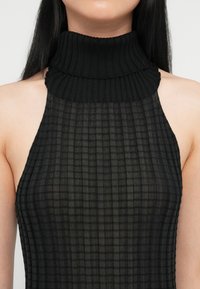 Μαύρη αμάνικη μπλούζα με ψηλό λαιμό, κατασκευασμένη από ριγέ, διαφανές ύφασμα με γεωμετρικό σχέδιο, διαθέτει διπλωμένο γιακά και ανοιχτούς ώμους.