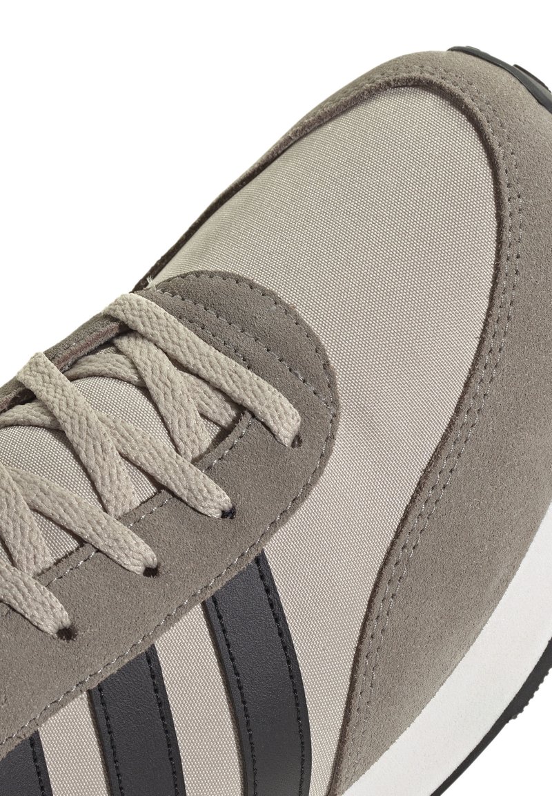 Close-up van de beige en taupe sneakerneus met textiel, suède overlays, beige veters en drie zwarte strepen aan de zijkant.