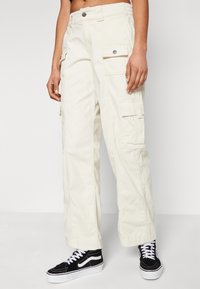 Cargo bukser i off-white stof, med sidelommer, afslappet pasform og knaplukning. Sammen med sorte sneakers.