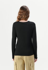 Zwarte lange mouw top met een ronde halslijn, gemaakt van een gladde stof, gecombineerd met lichtbeige cargo broeken met zijzakken.