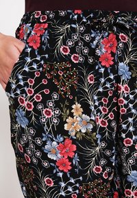 Black floral patterned pants featuring a drawstring waist, vibrant pink, blue, and white flowers, and side pockets for practicality.