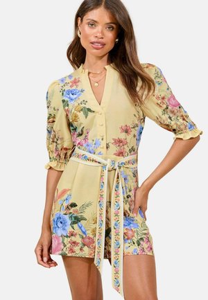 Floral mini dress in yellow with puff sleeves, featuring a button front, cinched waist, and a tie belt; decorated with various colorful flowers.