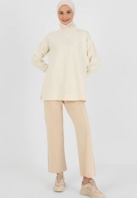 Cream-colored long-sleeve top with a high neckline, paired with beige wide-leg pants and light sneakers. The fabric appears soft and smooth.