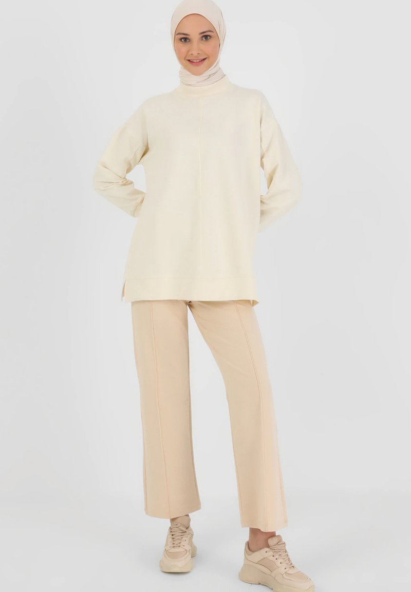 Cream-colored long-sleeve top with a high neckline, paired with beige wide-leg pants and light sneakers. The fabric appears soft and smooth.