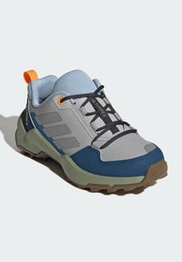 Grå og blå vandresko med overdel i mesh, gummisål, sorte snørebånd og orange accent. Har en forstærket tå og teksturerede detaljer.