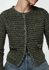 Cardigan vert texturé en tricot avec un col rond, une fermeture à boutons sur le devant et deux poches. Comprend des accents tressés et des boutons dorés.