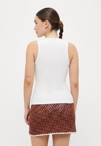 Top blanco sin mangas combinado con una mini falda marrón de ganchillo con un dobladillo con forma de olas, que muestra un intrincado patrón tejido.