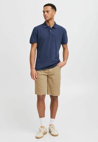 Marineblå poloshirt, khaki shorts, hvide sokker og beige sneakers. Glat tekstur, krave-design og afslappet pasform.