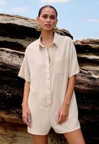 Bežna kratka obleka z gumbi, s kratkimi rokavi, z žepom na prsih, izdelana iz teksturirane tkanine, z velikimi svetlimi gumbi in sproščenim krojem.