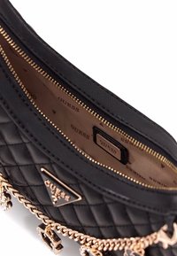 Borsa a tracolla nera trapuntata con hardware dorato e dettaglio a catena. L'interno presenta una fodera beige e dettagli con logo. Chiusura a zip.