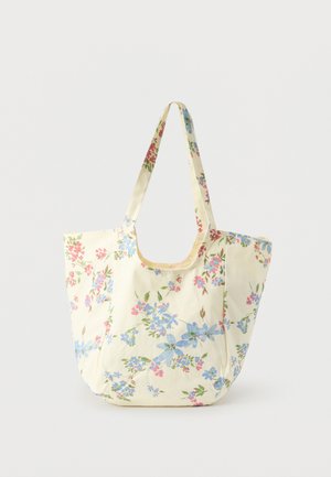 Kremfarvet taske med blå og lyserødt blomsterprint og lange håndtag, vist mod en ensfarvet hvid baggrund.