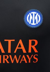 Μαύρη αθλητική φανέλα με μπλε και λευκό κεντημένο λογότυπο της Ίντερ Μιλάνο και μερικώς ορατό πορτοκαλί κείμενο χορηγού Qatar Airways.