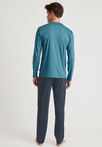 Langwerpige turquoise shirt met lange mouwen, gecombineerd met marineblauwe pyjamabroek met een vierkant patroon. Comfortabele stof, een relaxte pasvorm en een eenvoudig ontwerp.