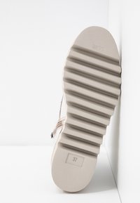 Beigenvärinen lenkkaripohja, jossa pystysuora uritettu kuvio. Kokoetiketti "37" ja minimalistinen muotoilu. Sileät reunat ja tasainen pohja.