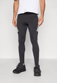 Svarta atletiska leggings med vita sidostripes, figurnära design gjord av stretchigt material, kombinerade med svarta sportskor.