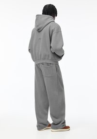 Szürke kapucnis sweatshirt, húzózsinórral és kenguruzsebbel, szürke melegítőnadrággal párosítva, hátsó zsebbel és laza illeszkedéssel.