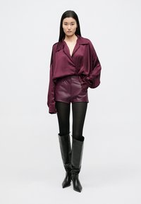 Nadrozměrná košile z vínového saténu, kožené šortky s vysokým pasem, černé punčochy a černé kozačky na podpatku po kolena. Jednoduchý a moderní design.