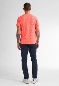 Neonrosa T-Shirt mit kleinen schwarzen Mustern, kombiniert mit marineblauen Hosen und weißen Sneakers; Kurzarm- und Rundhalsausschnitt-Design.
