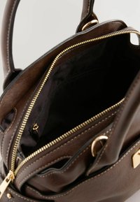Bruine leren handtas met gouden ritssluiting, zichtbaar zwart stoffen interieur en een klein binnenzakje met rits, twee handvatten zichtbaar.