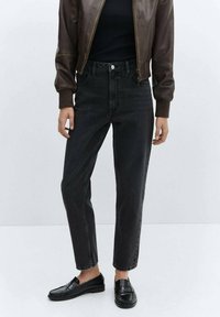 Jeans negros de cintura alta con un corte recto, que cuentan con cinco bolsillos y trabillas para el cinturón, combinados con una chaqueta bomber de cuero oscura y zapatos de slip-on.