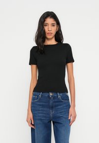 Μαύρο εφαρμοστό τοπ με κοντά μανίκια και στρογγυλή λαιμόκοψη, σε συνδυασμό με μπλε τζιν ψηλόμεσο με κλασικά κουμπιά και φερμουάρ.