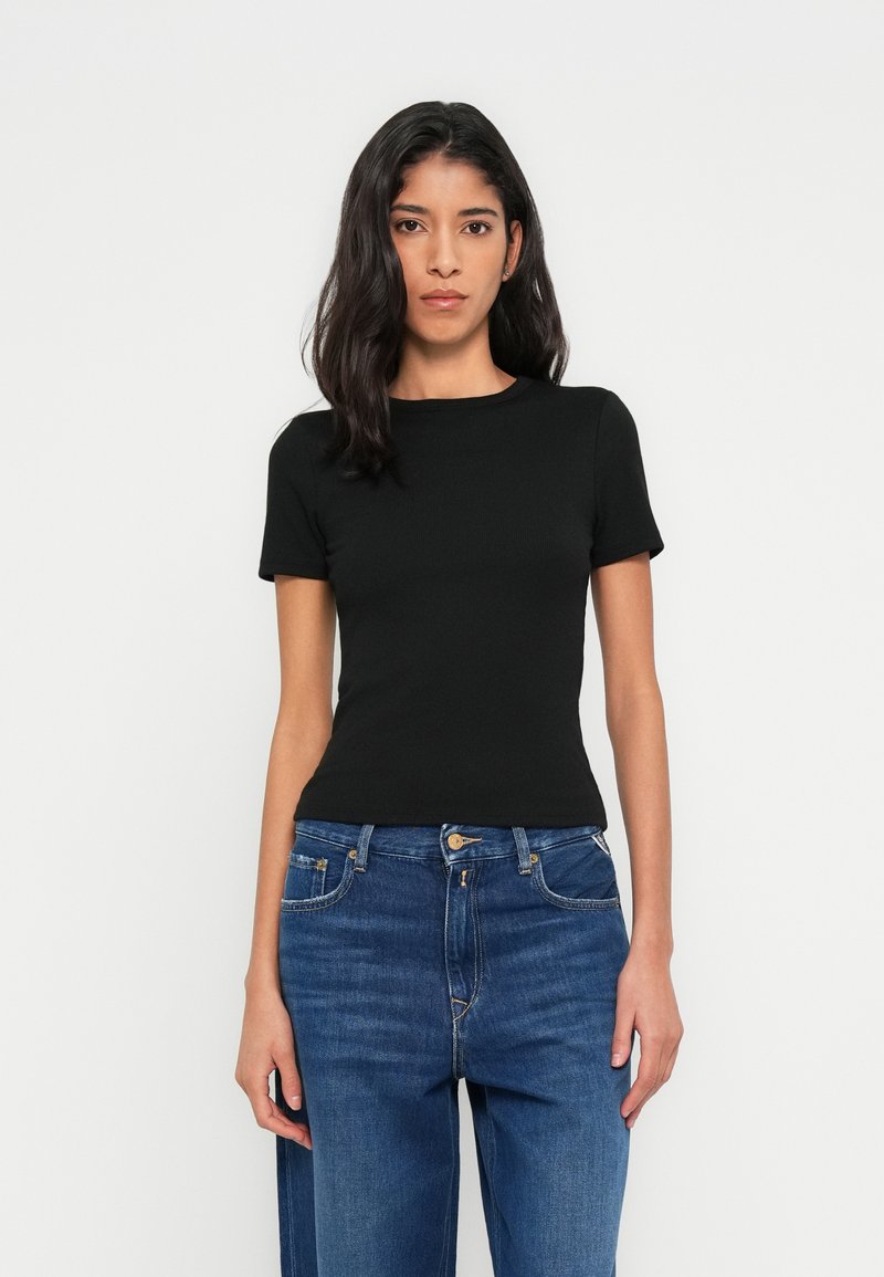 Μαύρο εφαρμοστό τοπ με κοντά μανίκια και στρογγυλή λαιμόκοψη, σε συνδυασμό με μπλε τζιν ψηλόμεσο με κλασικά κουμπιά και φερμουάρ.