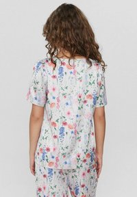 Top a maniche corte con motivo floreale su sfondo bianco, caratterizzato da fiori colorati in tonalità di rosa, blu e verde; tessuto leggero.