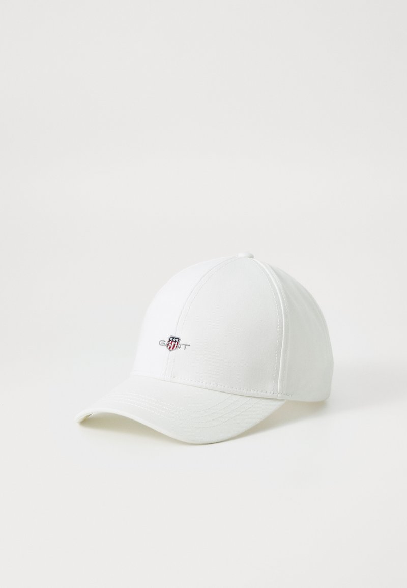 White baseball cap made of cotton. Features a curved brim and a small embroidered logo on the front with red, white, and blue accents.