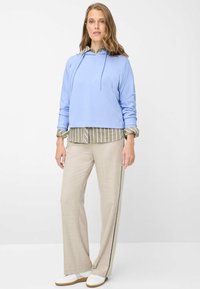 Felpa corta azzurro chiaro, camicia a righe beige sotto, pantaloni beige a gamba larga con striscia laterale nera e sneakers bianche.