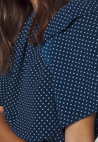 Mörkblå blus med vita prickar, med kragen och korta ärmar. Strukturerad tyg med en slät yta.