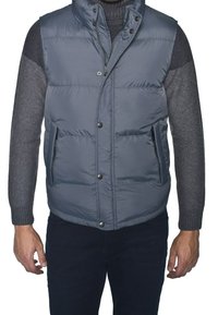 Graue gepolsterte Weste mit hohem Kragen, Druckknöpfen und zwei Seitentaschen. Strukturierte Strickärmel, die einen Farb- und Materialkontrast bieten.