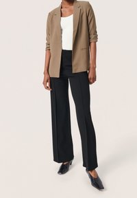 Brązowa marynarka z podwiniętymi rękawami, biały prążkowany top na ramiączkach, czarne spodnie o szerokich nogawkach i czarne buty na obcasie. Gładkie tekstury i dopasowany krój.