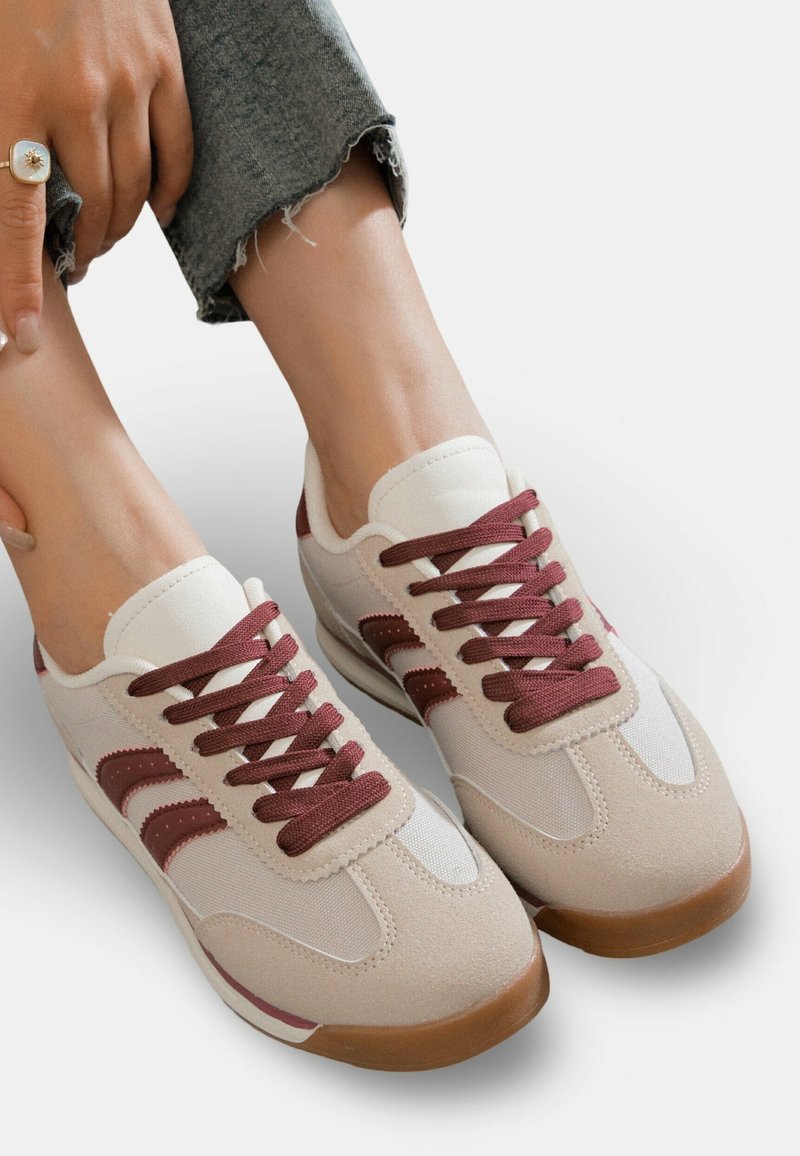 Chaussures de sport beige en suédine et maille, avec des lacets et des accents bordeaux, dotées d'une semelle en caoutchouc texturée et d'une languette rembourrée.