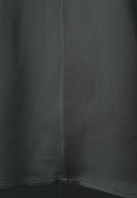 Gros plan sur un tissu gris foncé avec une couture verticale visible et un ourlet au bord inférieur.