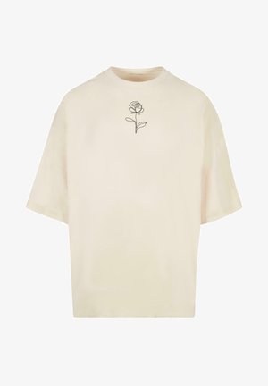 Camiseta de manga corta en color crema, hecha de un tejido suave. Presenta un dibujo minimalista de una rosa en negro en el pecho. Diseño de corte relajado.