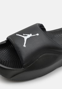 Juodos šlepetės su tekstūruotu viršumi, ant dirželio iškilusiu baltu Jumpman logotipu ir storu, kontūruotu padu.