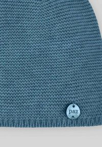 Bonnet tricoté en fil bleu doux et texturé avec un bord côtelé, doté d'une petite étiquette circulaire en relief portant la mention "paz".