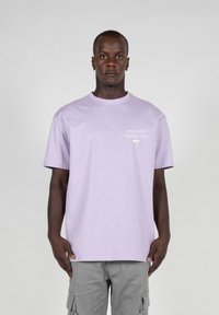 Purple cotton t-shirt with short sleeves and a crew neckline. Features white printed text on the front. Worn with gray cargo shorts.