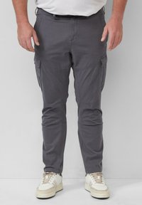 Grijze cargobroek met meerdere zijzakken, taps toelopende pasvorm en een lichtgewicht stof, gecombineerd met witte en beige sneakers.