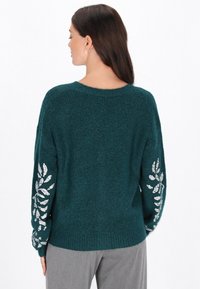 Suéter verde azulado con un diseño de punto texturizado, con mangas largas adornadas con un bordado de patrón de hojas plateadas en los puños.