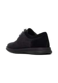 Zapato de ante negro con parte superior texturizada, puntera redondeada y cordones decorativos. Presenta una suela de goma flexible y un talón trasero reforzado.