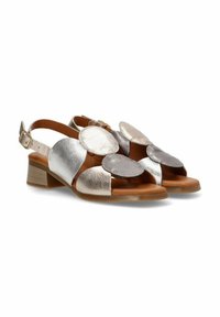 Sandalias plateadas y metálicas con diseño de recortes, detalles redondos y tacón bajo. Elaboradas en cuero y con una correa en el tobillo.