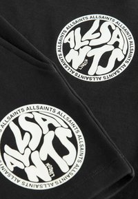 Črna bombažna majica s krožnim belim grafičnim motivom in napisom "ALLSAINTS" v igrivem pisavi. Napis vključuje lokacijo "London."