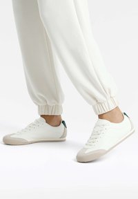 Fehér sneaker bézs gumitalppal és világoszöld sarokdíszítéssel. Simább bőrből készült felső rész, varrott részletekkel és fűzős elejével.